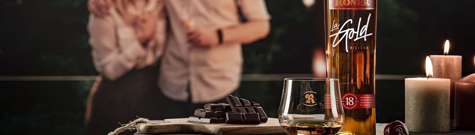 Roner Glas mit Grappa La Gold auf Brett Schokolade und Menschen dahinter